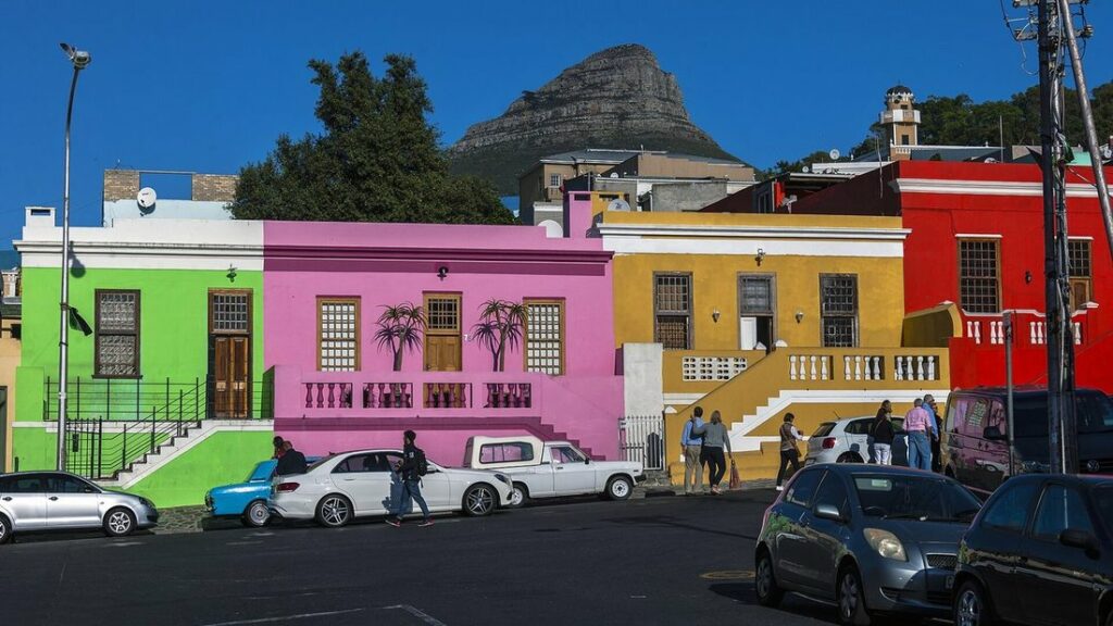 Maisons peintes en vert, rose, jaune et rouge le long d'une rue, avec la montagne Lion's Head au fond