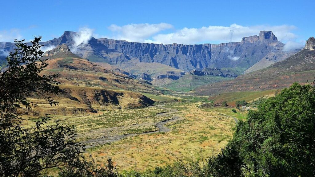 Vallée verte dominée par une longue paroi rocheuse, l'Amphithéâtre, sous un ciel bleu