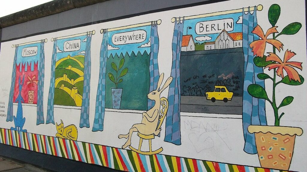 Fresque colorée sur un tronçon du Mur : un lièvre dans un fauteuil à bascule devant des fenêtres peintes, dont une avec une Trabant jaune