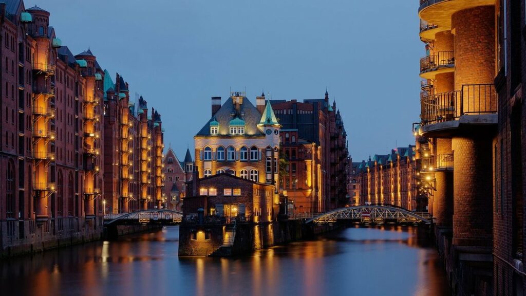 Entrepôts en briques rouges éclairés et reflétés dans un canal, avec le petit château d'eau au centre