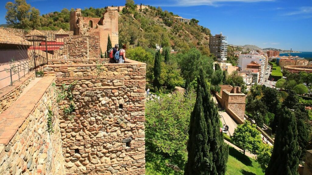 Murailles de pierre de l'Alcazaba de Málaga parmi les cyprès, avec la ville et la mer au fond