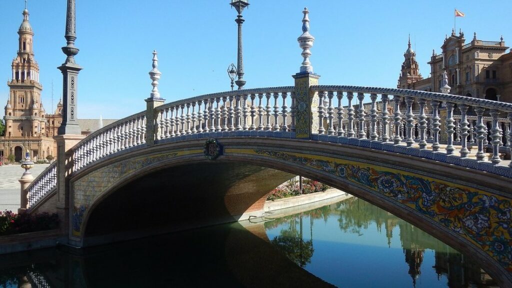 Pont de céramiques bleues et jaunes au-dessus du canal de la Plaza de España, avec des tours de brique au fond