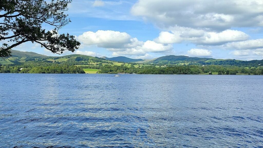 Le lac Windermere et les collines boisées du Lake District, sous un ciel bleu parsemé de nuages
