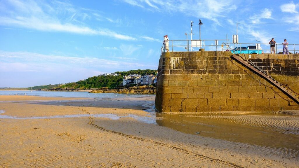 Jetée en pierre et plage de sable à marée basse dans le port de St Ives, sous un ciel bleu