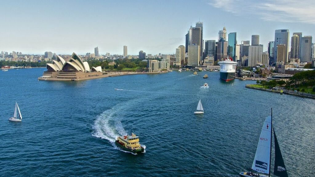 L'Opéra de Sydney sur sa pointe, des ferries et des voiliers sur la baie, et les tours du centre-ville au fond