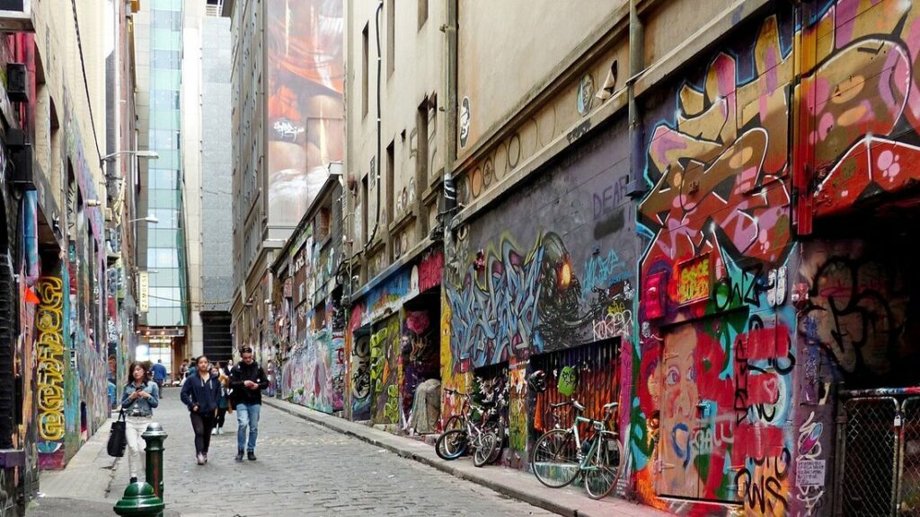 Ruelle étroite aux murs couverts de graffitis colorés, avec quelques passants au fond