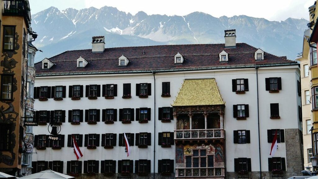 Le Toit d'Or doré sur la façade blanche d'un bâtiment d'Innsbruck, avec les montagnes derrière
