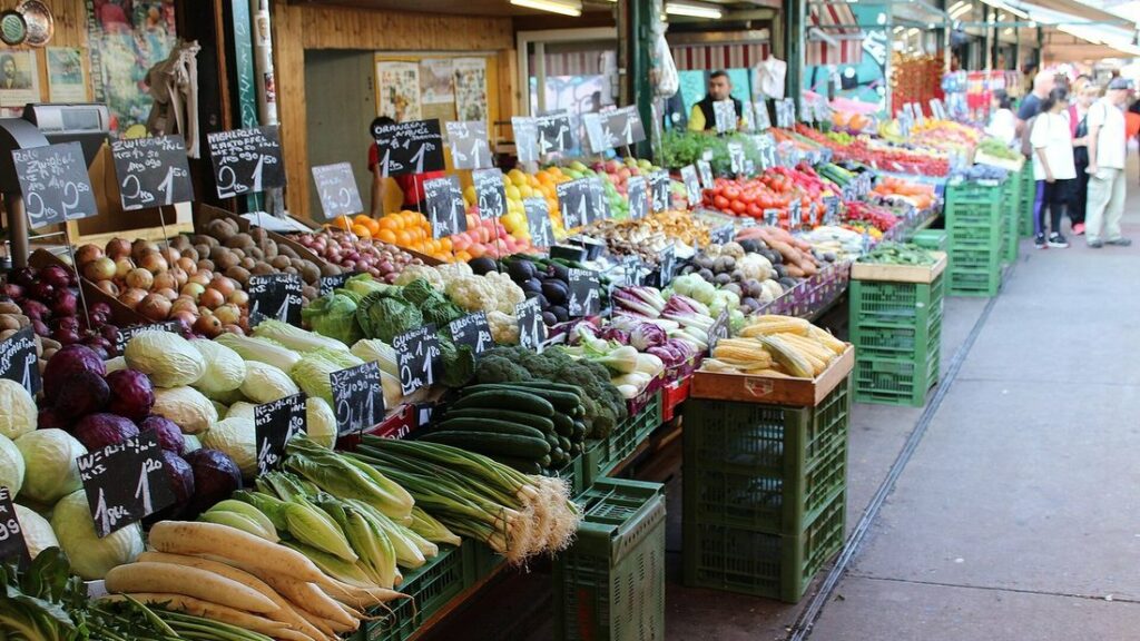 Allée de marché avec des étals de légumes frais, des cageots verts et des étiquettes d'ardoise