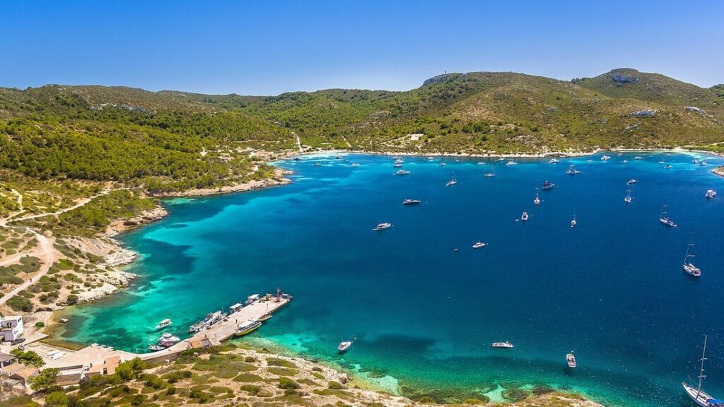 Baie de l'île de Cabrera aux eaux turquoise, avec un appontement et des voiliers au mouillage, au pied de collines boisées