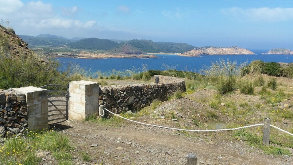 Sentier de terre entre des murets de pierre sèche, avec la côte nord de Minorque et la mer au loin