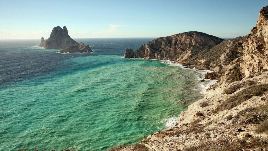 Îlot rocheux d'Es Vedrà au large d'une côte de falaises claires, avec une mer vert et bleu