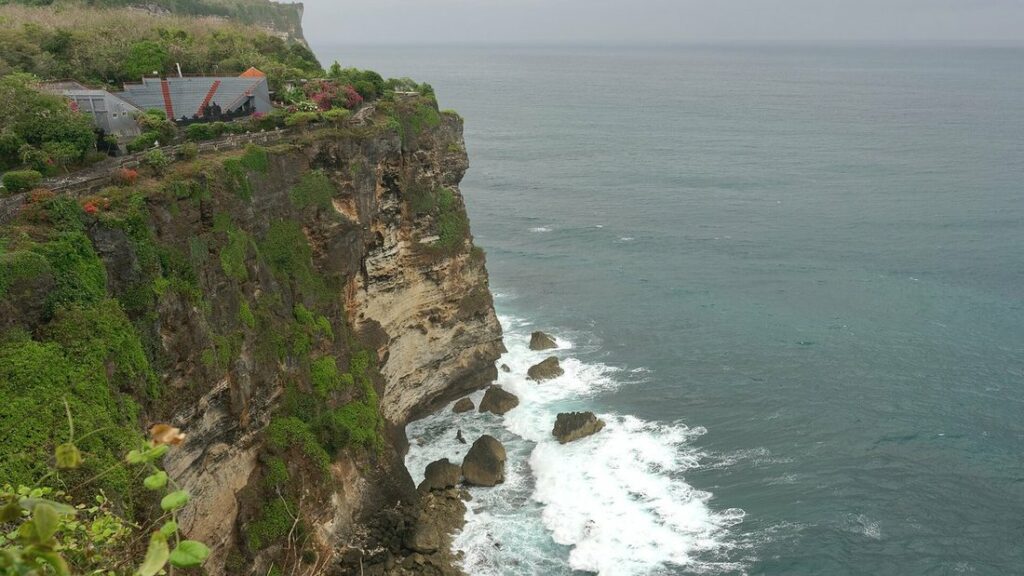 Haute falaise verte et ocre tombant dans l'océan, avec des vagues blanches à son pied