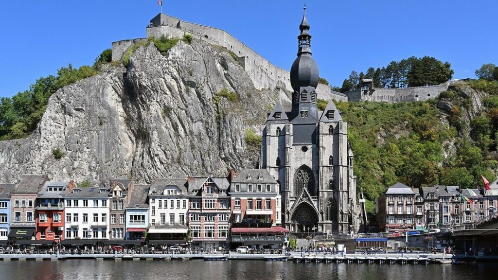 La collégiale à clocher bulbeux au pied de la falaise surmontée de la citadelle, sur les bords de la Meuse à Dinant