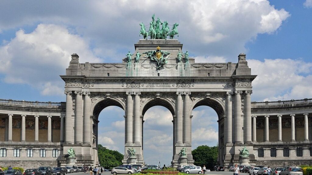 Grand arc de triomphe à trois baies surmonté d'un quadrige en bronze vert, sous un ciel bleu nuageux