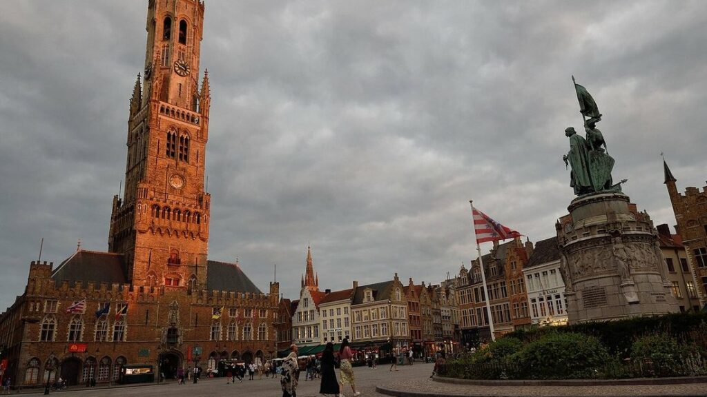 Le beffroi en brique et un monument à statues sur la place du Markt, sous un ciel gris et nuageux