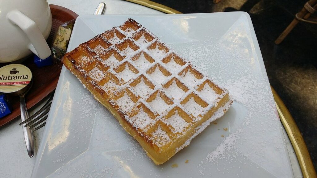 Gaufre rectangulaire saupoudrée de sucre glace sur une assiette blanche, posée sur une table de café