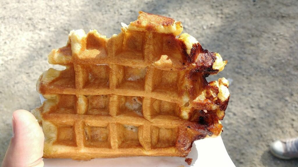 Gaufre de Liège ronde aux bords caramélisés, croquée, tenue à la main