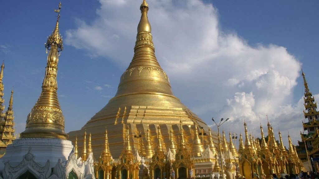 Stupa doré de la pagode Shwedagon entouré de petits sanctuaires dorés, sous un ciel bleu aux nuages blancs