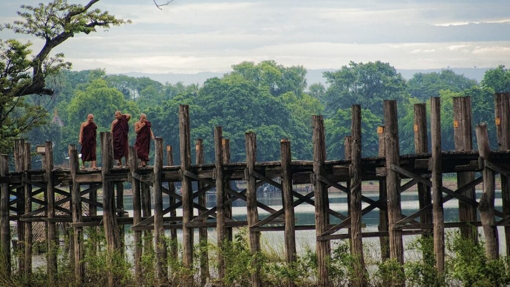 Pont de teck U Bein sur ses nombreux pilotis, avec des moines en robe pourpre qui le traversent, au bord d'un lac