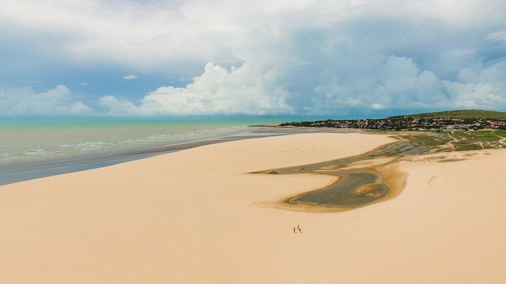 Vue aérienne d'une grande dune de sable clair qui domine le rivage et un village à Jericoacoara