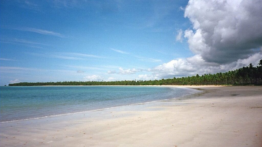Longue plage de sable clair frangée de cocotiers sous un ciel bleu mêlé de nuages, à Morro de São Paulo