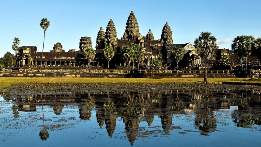 Les cinq tours d'Angkor Wat dominant la végétation, avec leur reflet dans un bassin sous un ciel bleu