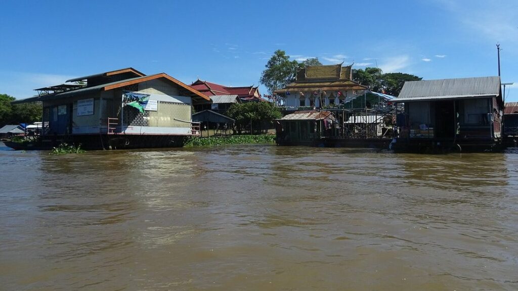Maisons sur pilotis d'un village flottant au bord d'une eau brune, sous un ciel bleu, sur le lac Tonlé Sap