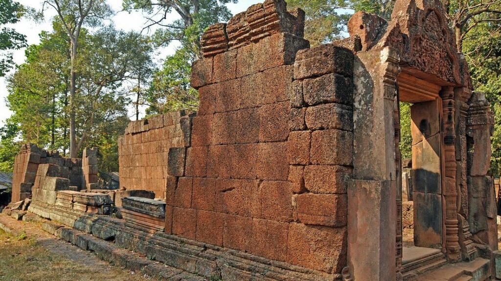 Mur et porte de grès rose au fronton sculpté, parmi les arbres, à l'entrée du temple de Bantéay Srei
