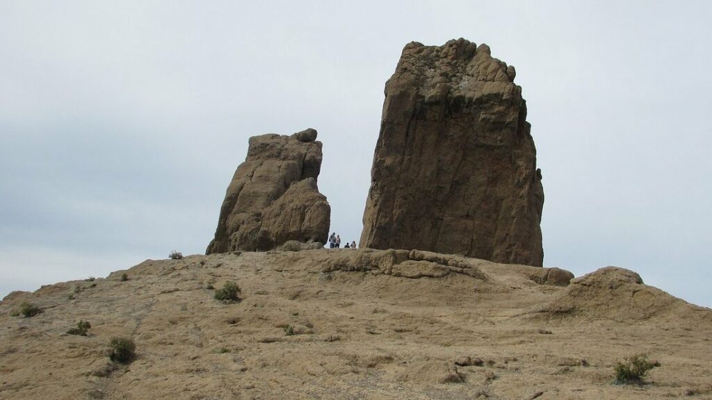 Roque Nublo, deux masses rocheuses dressées sur une crête sous un ciel nuageux, avec quelques visiteurs au pied