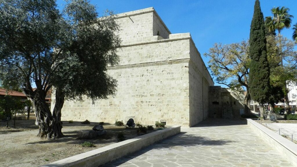 Façade en pierre claire du château médiéval de Limassol, entourée d'arbres, sous un ciel bleu