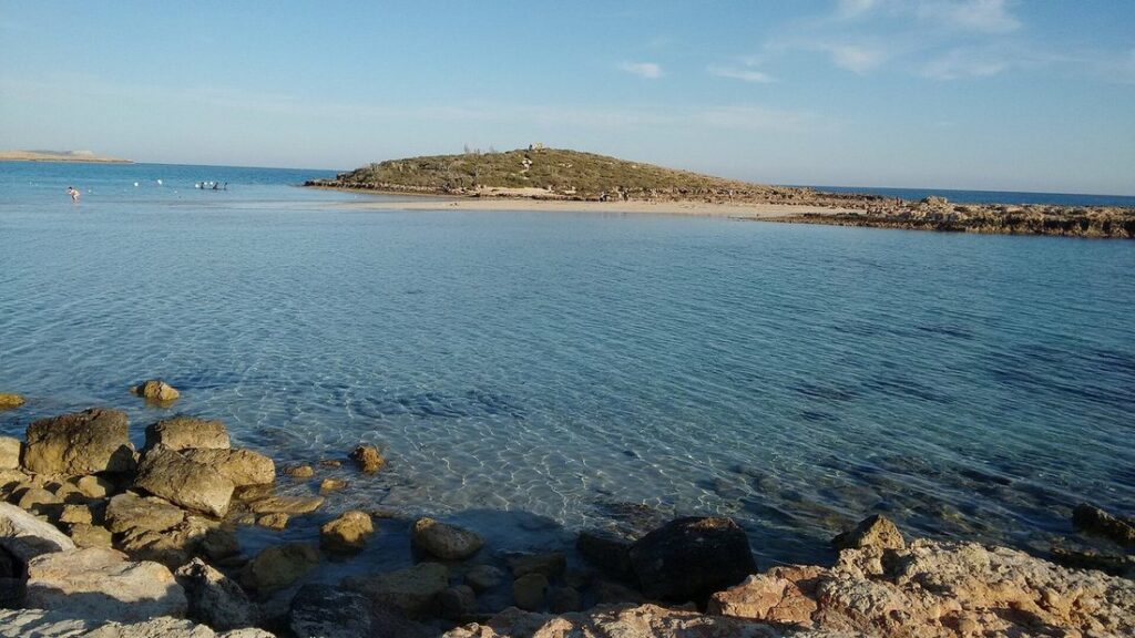 Eau claire et peu profonde de Nissi Beach avec un îlot en arrière-plan et des rochers au premier plan