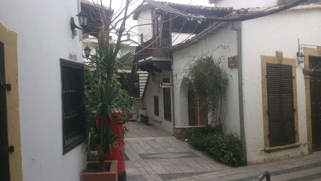 Ruelle pavée entre des maisons blanches à volets bruns, avec des plantes en pot, dans le quartier de Laïki Geitonia