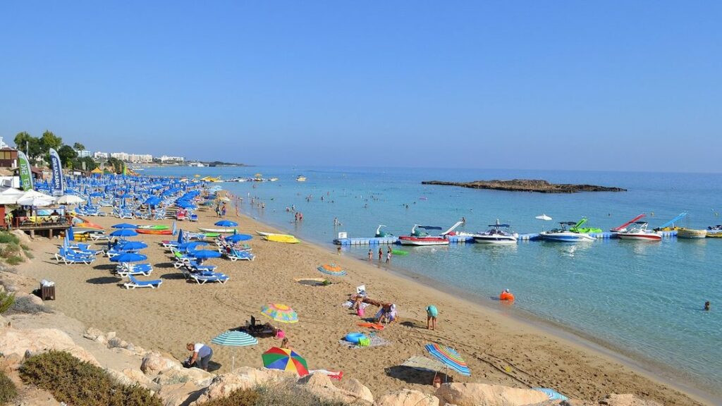 Plage de sable de Fig Tree Bay avec parasols bleus, baigneurs, bateaux amarrés et eau turquoise