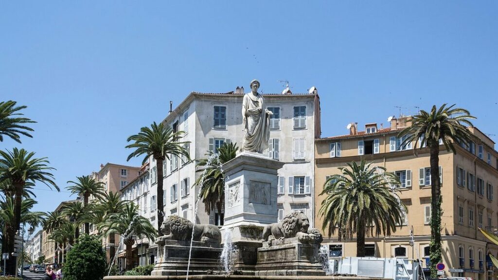 Place Foch à Ajaccio : statue de Napoléon, fontaine aux lions, palmiers et façades ocre sous un ciel bleu