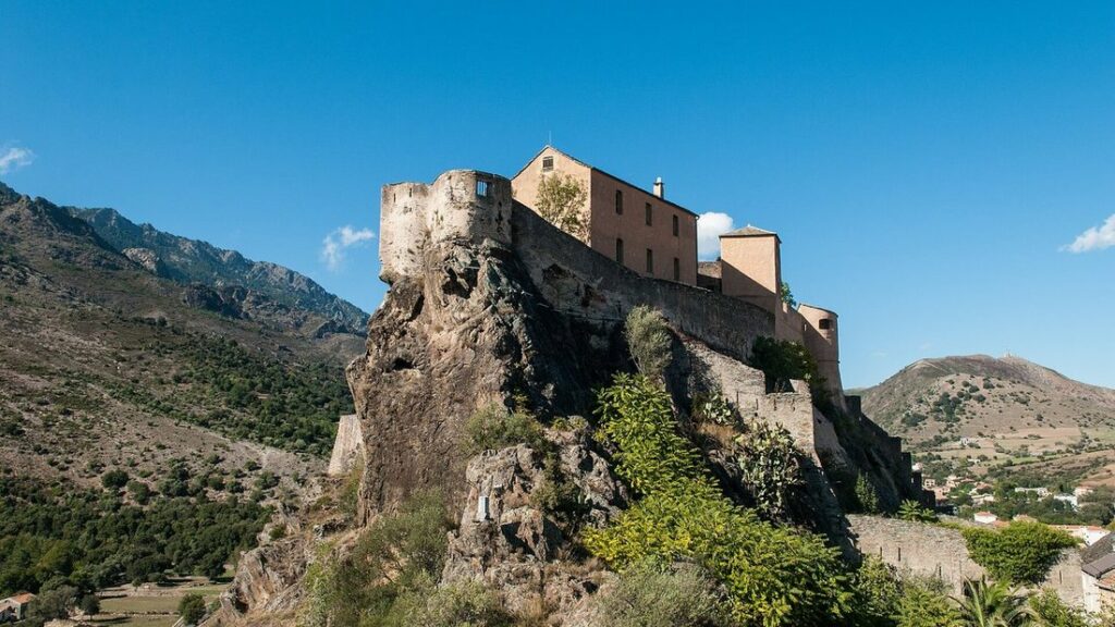 Citadelle de Corte sur son éperon rocheux, avec les montagnes en arrière-plan sous un ciel bleu