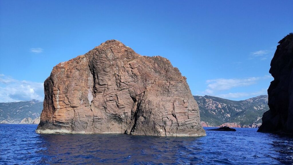 Gros rocher rougeâtre émergeant de la mer bleue, sur la côte de la réserve de Scandola