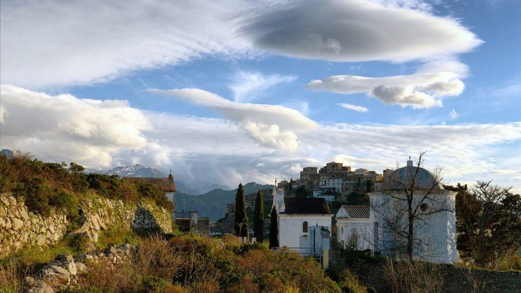 Bâtiments blancs au premier plan et maisons de pierre du village de Sant'Antonino sur sa colline, sous de gros nuages