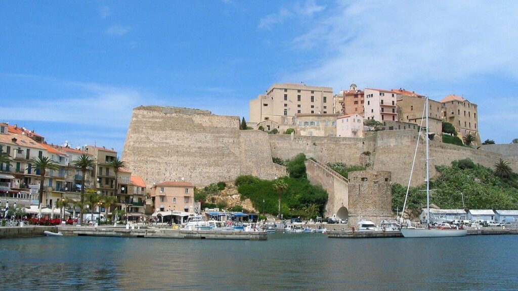 Citadelle de Calvi dominant le port, avec ses remparts de pierre, ses maisons colorées et un voilier à quai