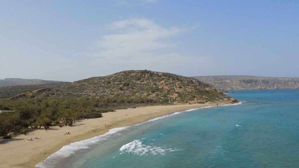 Plage de sable clair de Vai, eau turquoise et collines couvertes de palmiers sauvages en arrière-plan