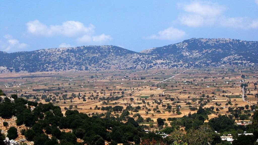 Plaine cultivée du plateau de Lassithi, entourée de montagnes rocailleuses sous un ciel avec quelques nuages