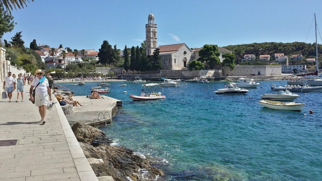 Quai de Hvar en bord de mer avec le clocher du monastère franciscain, des barques et une eau turquoise