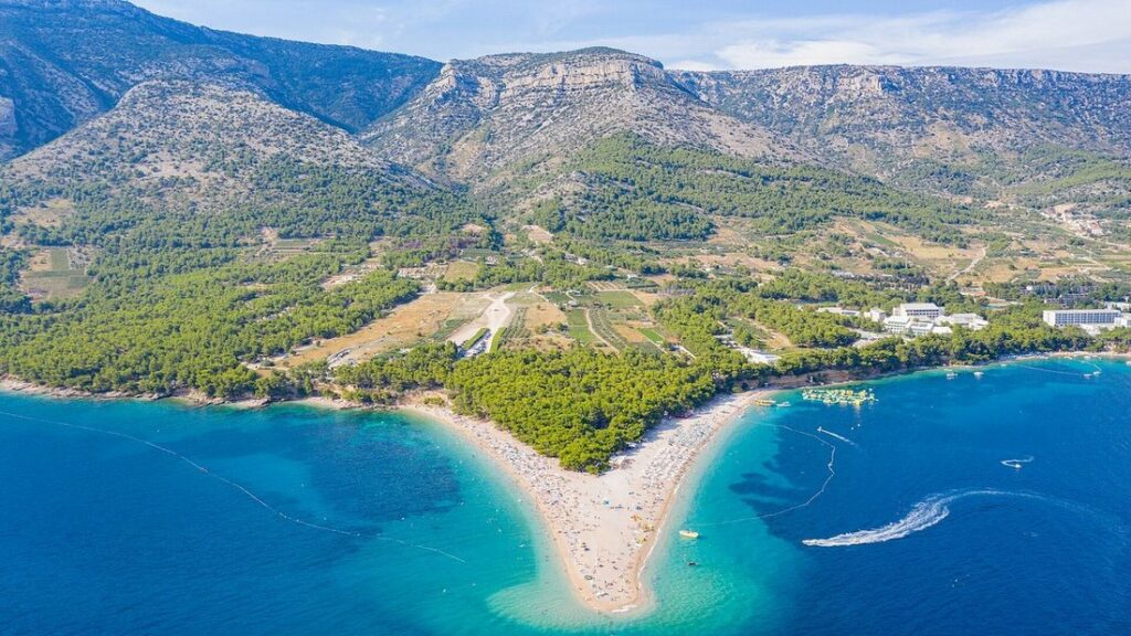 Vue aérienne de la langue de galets de Zlatni Rat, entourée d'eau turquoise, avec les montagnes de l'île de Brač derrière