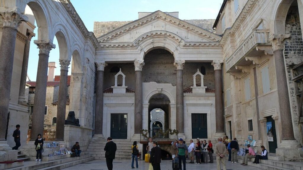 Le péristyle du palais de Dioclétien à Split, ses colonnes de pierre, son porche central et quelques visiteurs sur la place