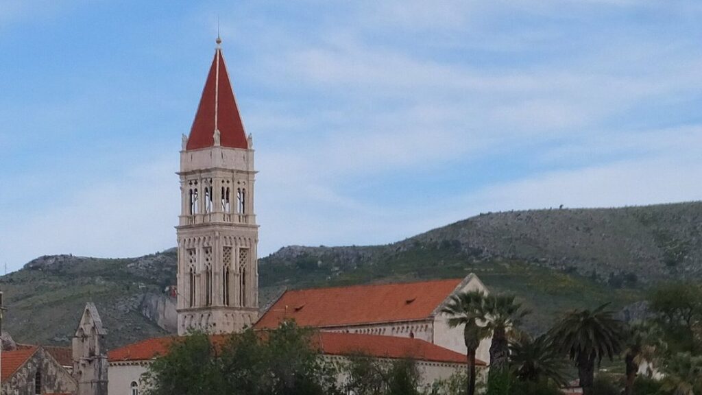 Clocher de la cathédrale Saint-Laurent dominant les maisons à toits de tuiles de Trogir, avec une colline derrière