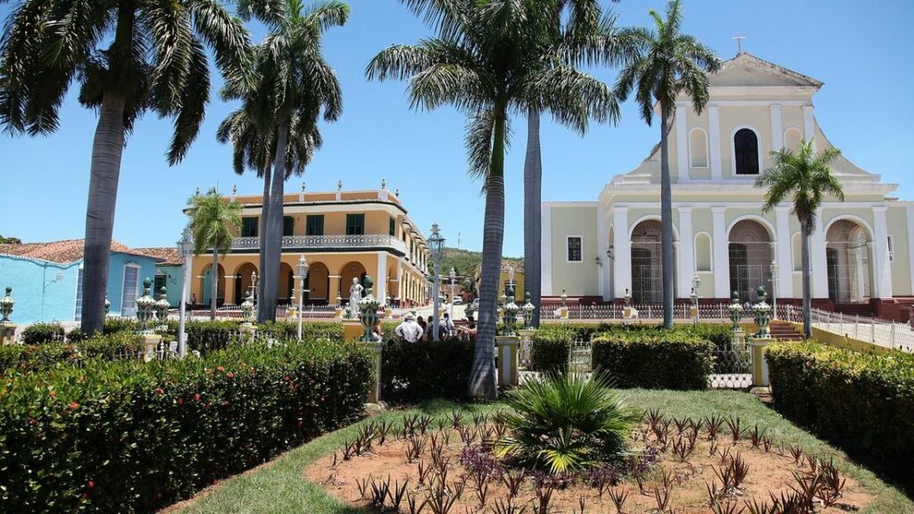 Palmiers et maisons colorées devant une église blanche sur la Plaza Mayor de Trinidad