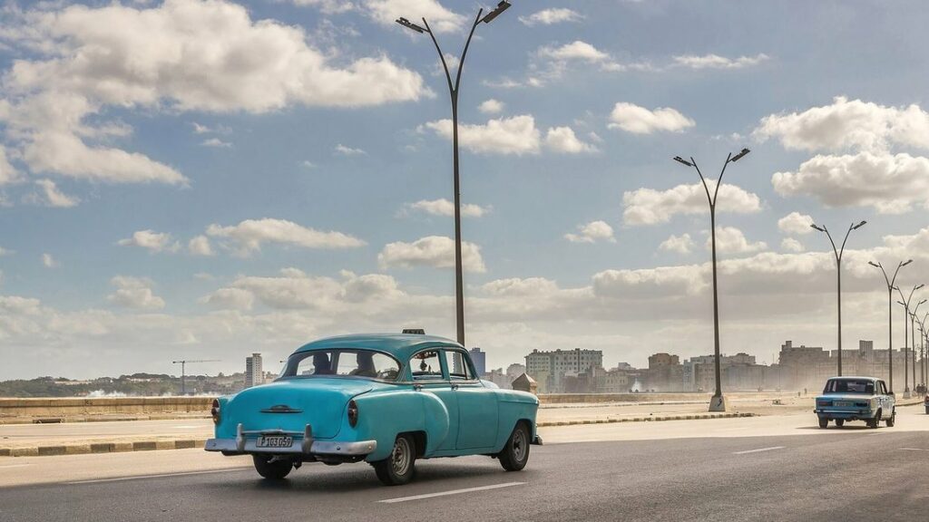 Voiture américaine ancienne turquoise roulant le long du Malecón, sous des lampadaires et un ciel nuageux