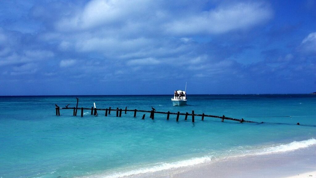 Eau turquoise et pilotis de bois dans la mer, sous un ciel bleu, sur la plage d'Ancón