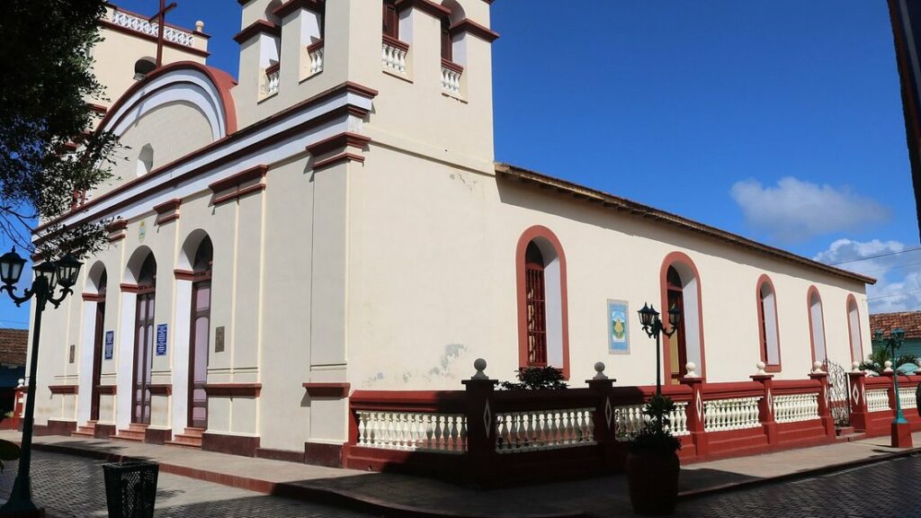 Cathédrale aux murs crème et aux bordures rouges, avec ses arcades et son clocher, sous un ciel bleu