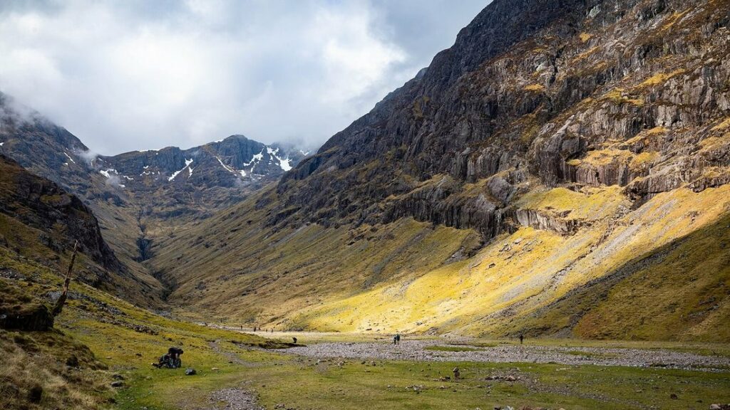 Vallée encaissée aux pentes d'herbe éclairées par le soleil, entre des montagnes sombres, à Glen Coe