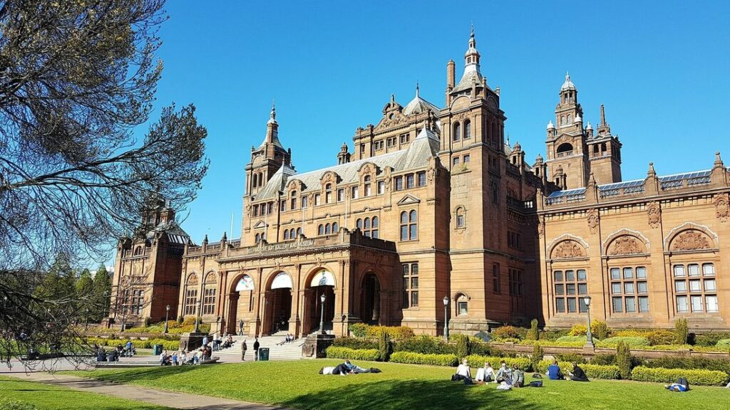 Façade en grès rouge du musée Kelvingrove, avec ses tours, sa pelouse et quelques visiteurs